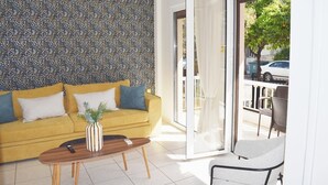 Ein modernes Wohnzimmer mit einem gelben Sofa, einem Couchtisch und einem grauen Sessel. Eine strukturierte Wand und eine Glastür zu einem Außenbereich sind zu sehen.