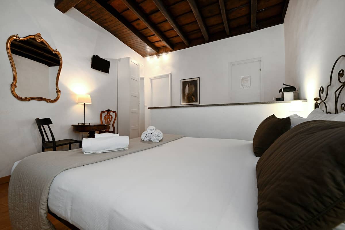 A hotel room with a large bed, a wooden headboard, a bedside table with a lamp, a chair, a mirror, and a framed picture on the wall.