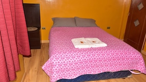 Una cama con una colcha rosa estampada, dos almohadas y dos toallas dobladas sobre la cama.