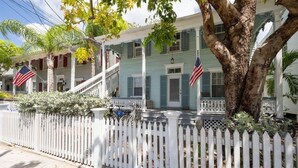 A two-story house with a white picket fence, a porch, and American flags. - Large 1 bedroom condo in the historic area of Key West! (Key West)