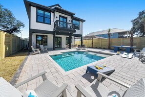 A two-story house with a swimming pool, outdoor seating, and a fenced backyard. - "White Heron" - Perfectly Located on the West End of Panama City Beach w/ Private Pool + easy 5 minute walk to the Beach! (Panama City Beach)