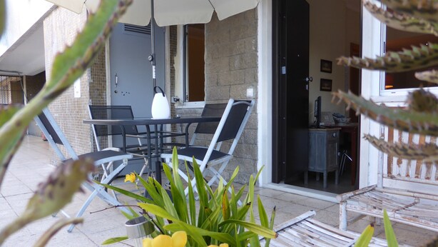 Une terrasse extérieure avec une table et des chaises, un parasol blanc et un pot de fleurs contenant des fleurs jaunes.