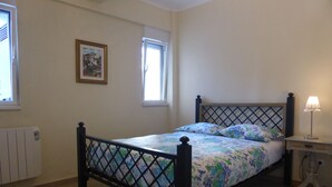 Une chambre à coucher comprenant un lit, une table de chevet, une lampe, un radiateur, une fenêtre et un tableau encadré accroché au mur.