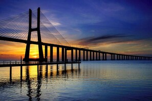 Eine Brücke mit Hängekonstruktion, die über ruhiges Wasser führt, mit einem Sonnenuntergang im Hintergrund.