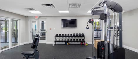 A gym with exercise equipment, a bench, dumbbells, and a television on the wall.