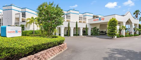 A hotel with a modern design, featuring a welcoming sign, a well-maintained garden, and a clear sky.