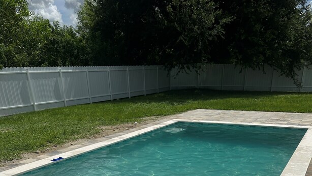 Ein rechteckiger Pool mit klarem Wasser, umgeben von einer gefliesten Terrasse und einem weißen Zaun.