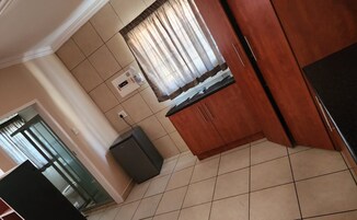 Una cocina con armarios de madera, suelo de baldosas y ventana con cortinas.