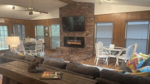 A cozy living room with a brick fireplace, a flat-screen TV, a wooden coffee table, and a comfortable sofa.