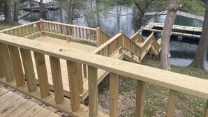 A wooden deck with a railing overlooking a body of water, surrounded by trees and a small dock.