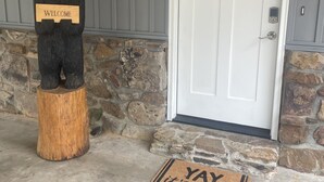 A wooden bear statue with a welcome sign, a white door, and a doormat with a message.