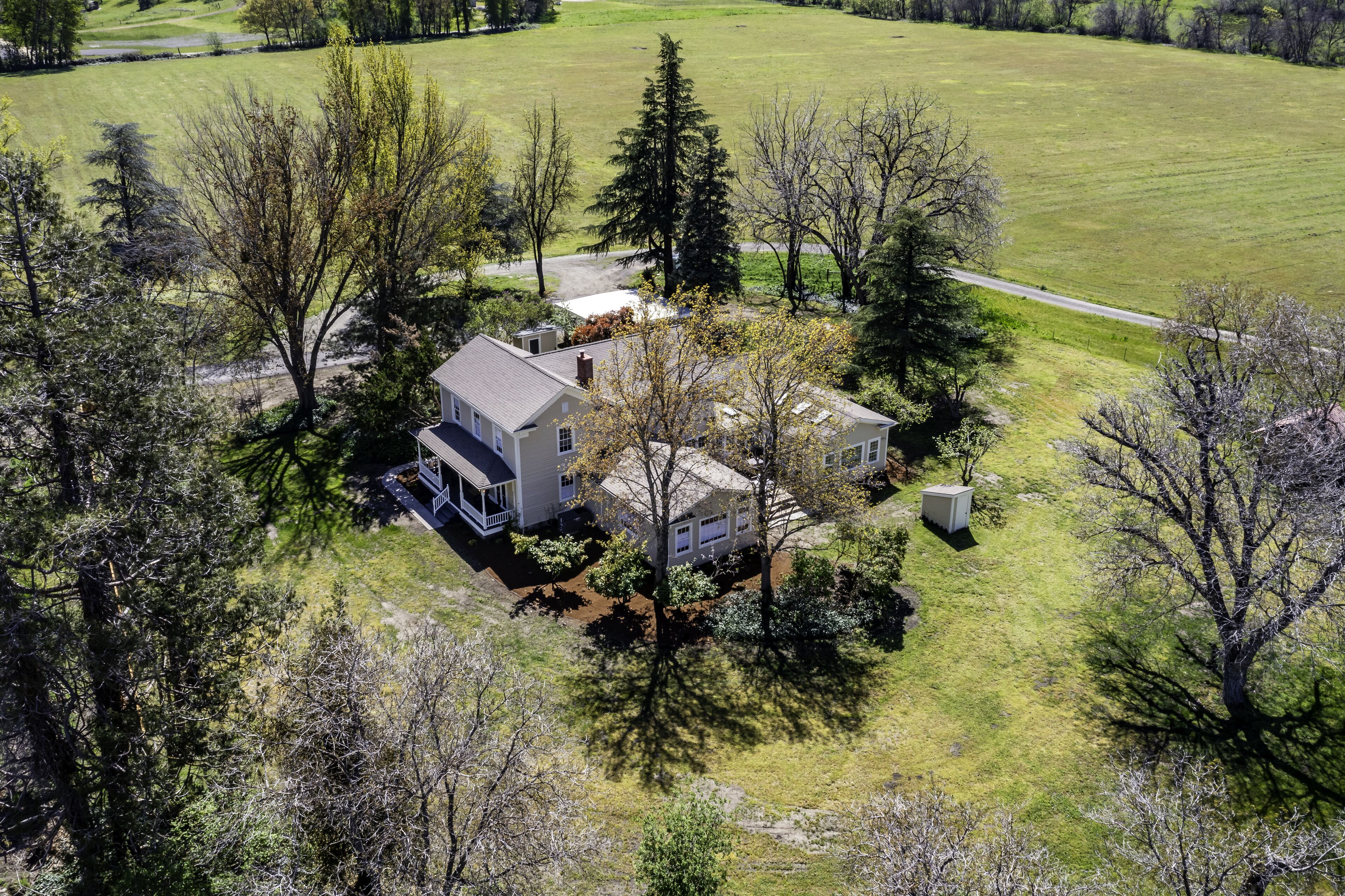 Une maison à deux étages avec un grand jardin à l’avant, entourée d’arbres et d’un champ d’herbe.