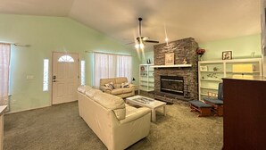 Un salon avec une cheminée en pierre, un canapé beige et un ventilateur de plafond.