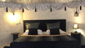 Quarto com uma cama, duas mesas de cabeceira, uma luminária e teto com tecido drapeado.