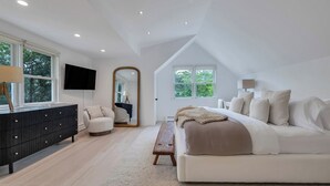 Un dormitorio moderno con una cama grande, un sofá, un televisor y un espejo.