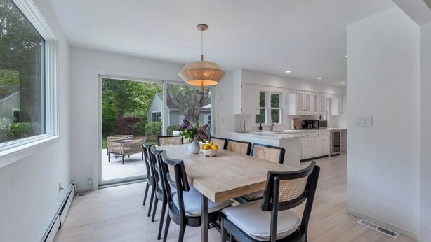 Una cocina moderna con armarios blancos, una isla grande y una zona de comedor con una mesa y sillas de madera.