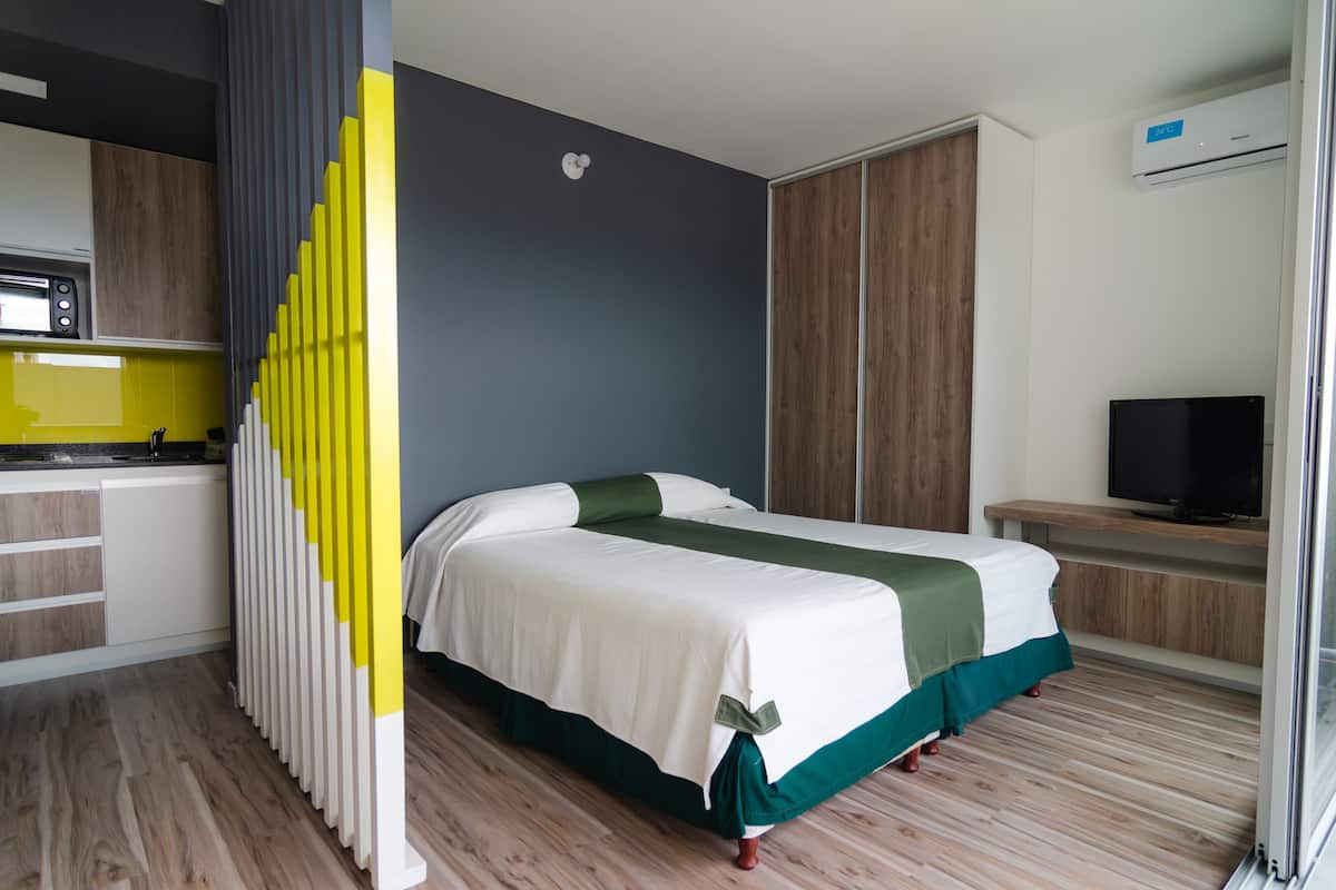 Una habitación de hotel moderna con una cama, un televisor, una kitchenette y una puerta corrediza.