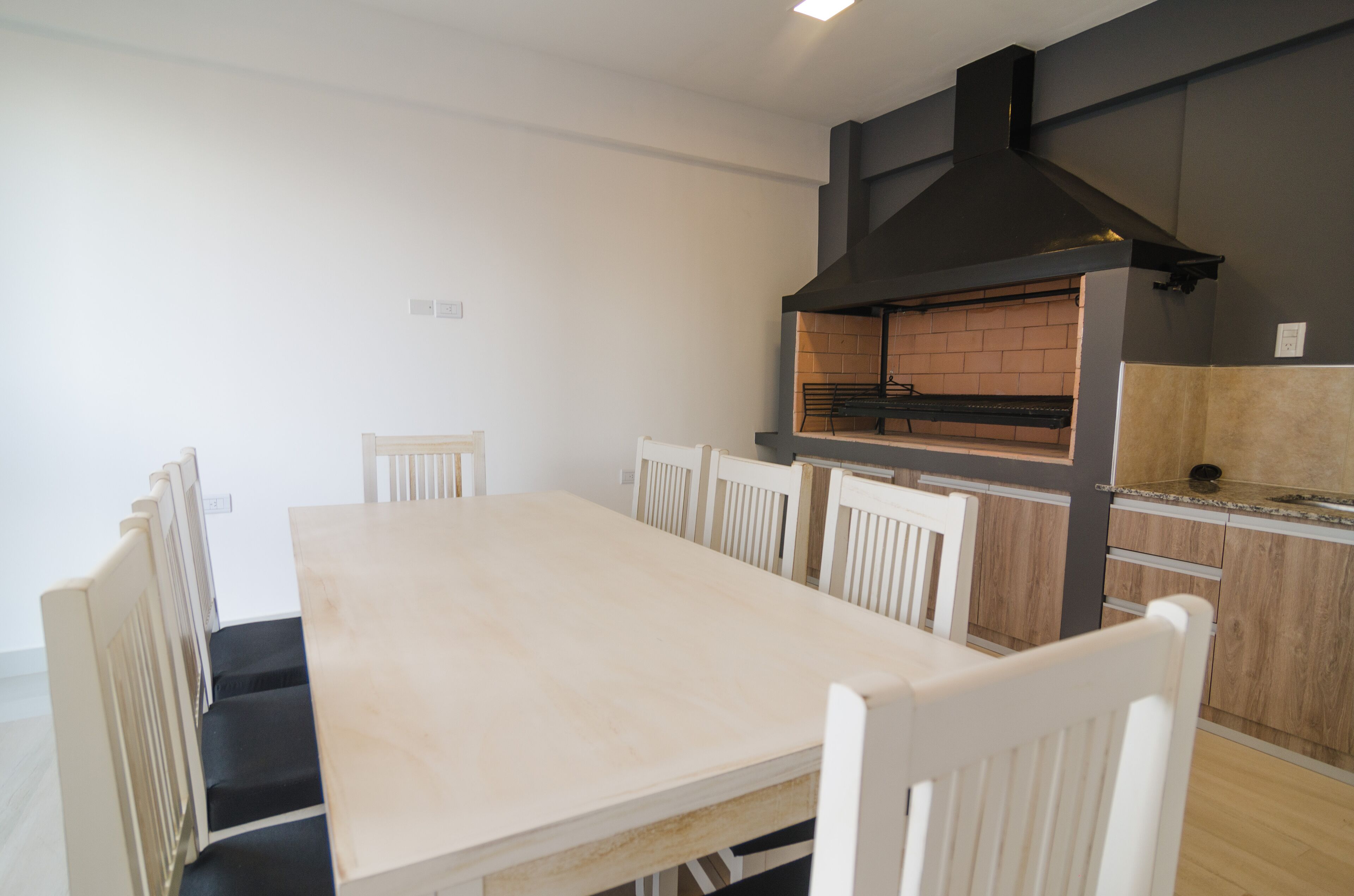 Un comedor con una mesa larga y sillas blancas, un horno de ladrillo y una cocina moderna con armarios de madera.