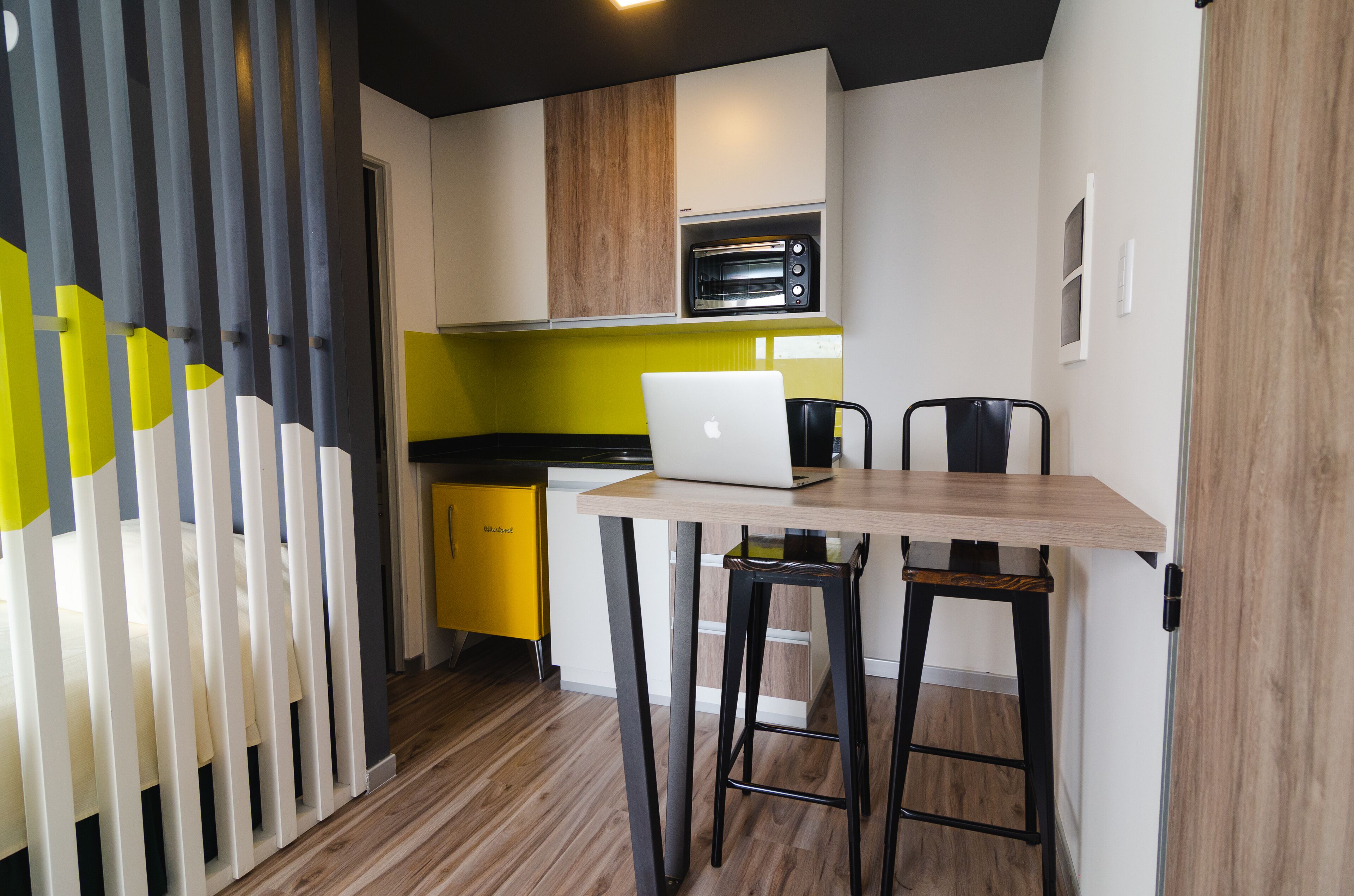 A compact kitchen with a wooden table, a laptop, and a toaster oven.