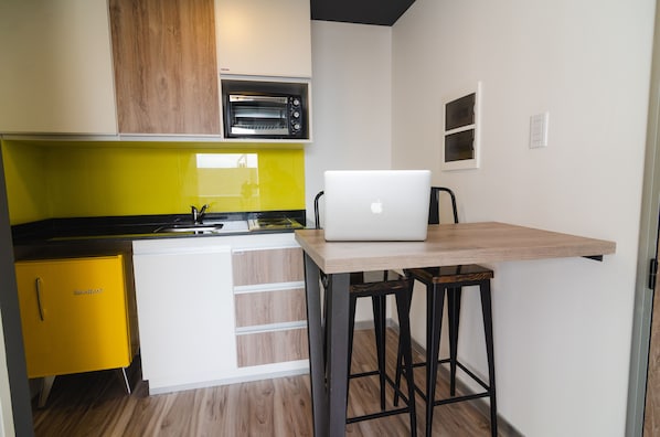 Una cocina compacta con horno integrado, un armario amarillo y una mesa de madera con una computadora portátil.