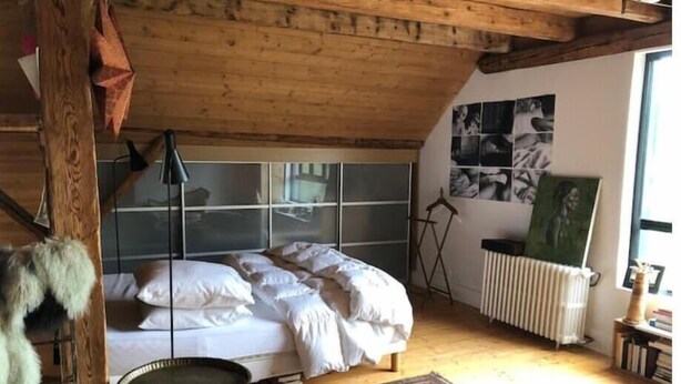 A bedroom with a bed, a small table, a radiator, and a wall with framed pictures.