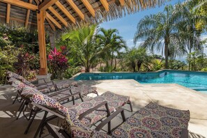 A poolside area with lounge chairs and a thatched roof structure. - Piece of Paradise in Manuel Antonio 7 Minutes to the Beach! Casa Colibri (Quepos)