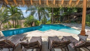 A swimming pool with lounge chairs under a thatched roof, surrounded by tropical vegetation. - Piece of Paradise in Manuel Antonio 7 Minutes to the Beach! Casa Colibri (Quepos)