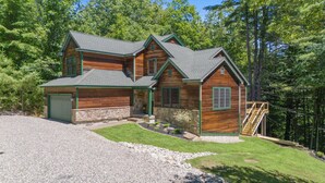 Eine zweistöckige Blockhütte mit Steinuntergrund, einer Veranda und einer Steinschmalseite.