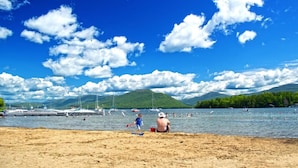 Ein Strand mit Booten, badenden Personen und Bergen im Hintergrund.