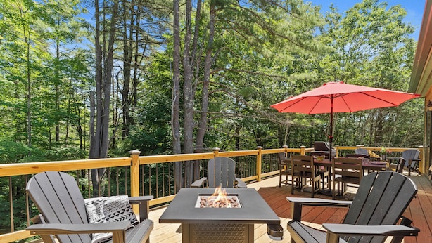 Eine Terrasse mit Adirondack-Stühlen, einem Tisch und einer Feuerstelle sowie einem roten Sonnenschirm.