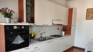 A modern kitchen with white cabinets, a black oven, a sink, and a stove. There are potted plants on the counter.