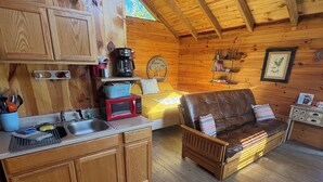 A cozy cabin interior with wooden walls, a kitchen area, a dining table, and a leather sofa. - Romantic Log Cabin w/ King Bed & Free Parking (Columbia)