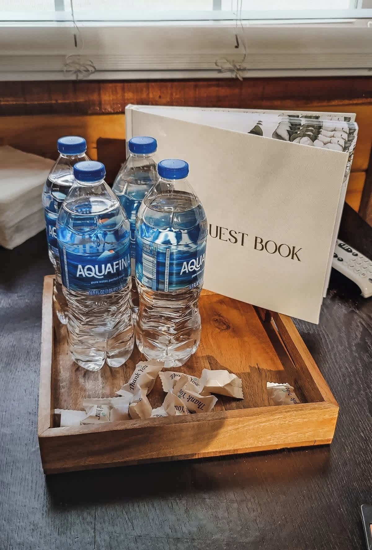 Un plateau en bois contenant quatre bouteilles d’eau Aquafina et un livre d’or, posés sur une table.