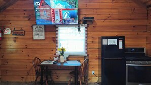 A cabin interior with a wooden interior, a dining table with chairs, a small kitchen area with a stove and refrigerator, and a television mounted on the wall. - Romantic Log Cabin w/ King Bed & Free Parking (Columbia)