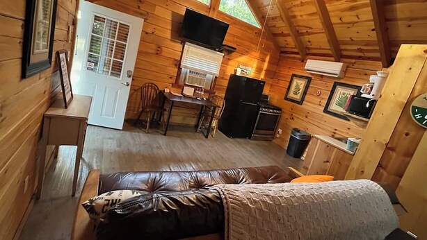 A cozy cabin with a wooden interior, a dining area, a kitchenette, and a bed with a view of the outdoors. - Romantic Log Cabin w/ King Bed & Free Parking (Columbia)