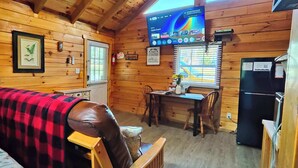 A cozy cabin with a wooden interior, a television mounted on the wall, a dining table, and a refrigerator. - Romantic Log Cabin w/ King Bed & Free Parking (Columbia)