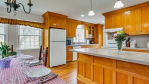 A kitchen with wooden cabinets, a central island, and a dining area with a checkered tablecloth. - Historic Farmhouse in Layton w/ Deck! (Layton)