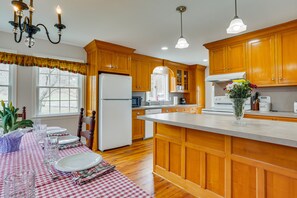 Una cocina con armarios de madera, un refrigerador, una mesa de comedor con platos y vasos, y una araña.