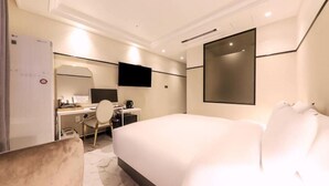 A modern hotel room with a large bed, a desk with a chair, a flat-screen TV, and a large mirror.