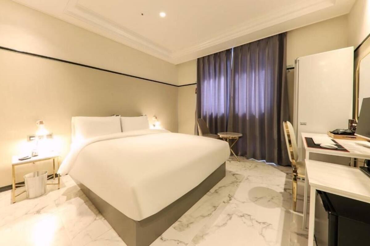 Une chambre d’hôtel avec un grand lit, un bureau avec une chaise, une petite table et un miroir.