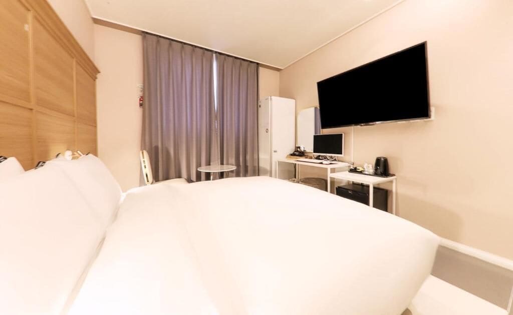 Une chambre d’hôtel avec un grand lit, un bureau avec un ordinateur, un téléviseur à écran plat et une fenêtre avec des rideaux.