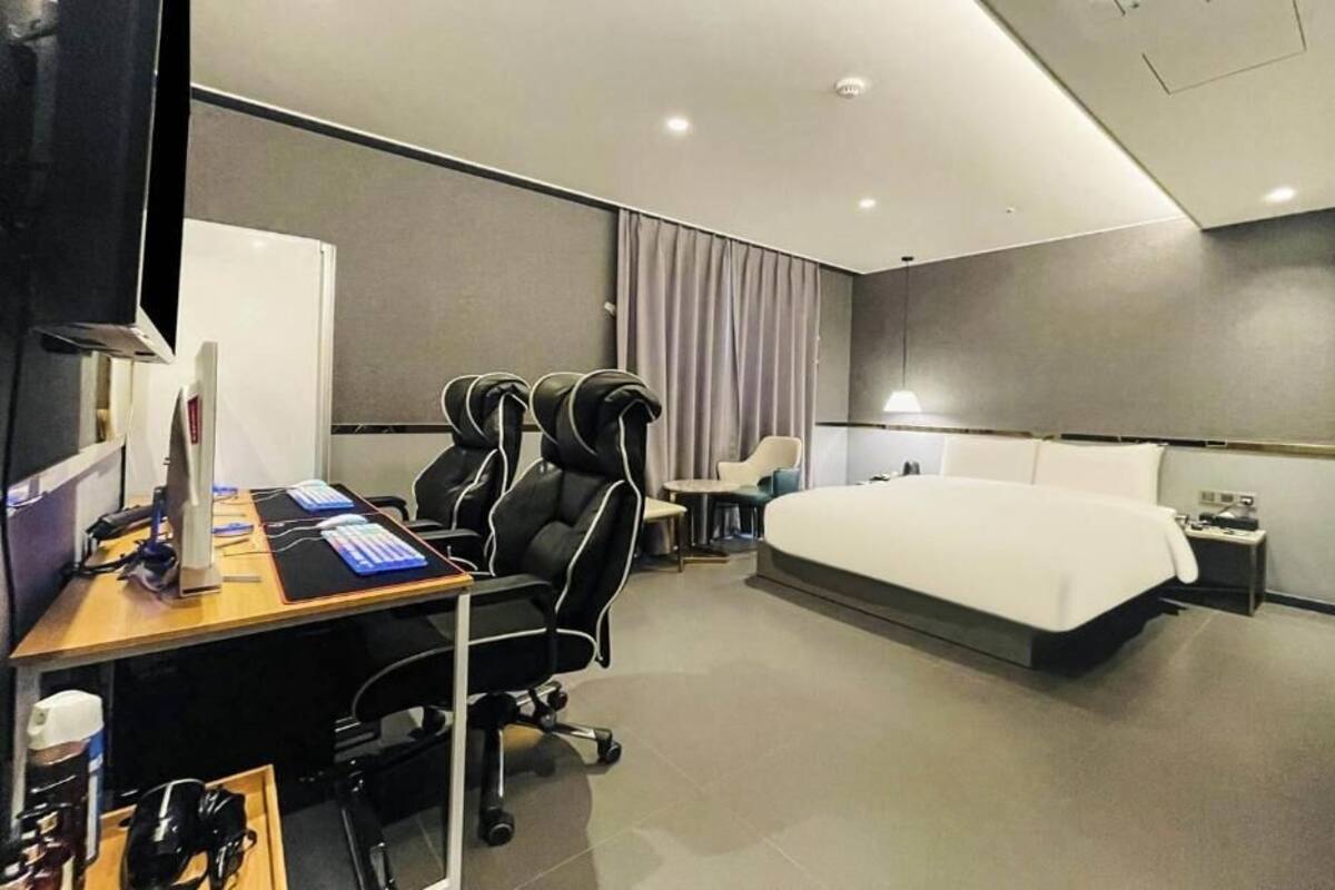 Une chambre d’hôtel moderne équipée d’un bureau, de deux fauteuils massants, d’un lit et d’une petite table.