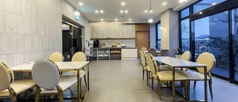 Un espace de restauration moderne avec des tables et des chaises, une cuisine en arrière-plan et de grandes fenêtres offrant une vue dégagée.