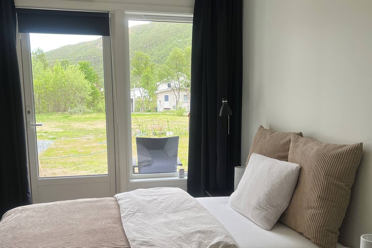 Une chambre d’hôtel avec un lit, une chaise, une lampe et une vue sur un jardin et des bâtiments à l’extérieur.