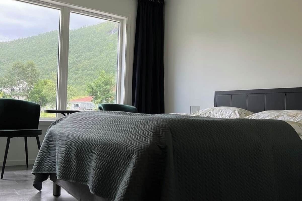 Une chambre à coucher comprenant un lit, une chaise, une table et une fenêtre donnant sur une forêt.