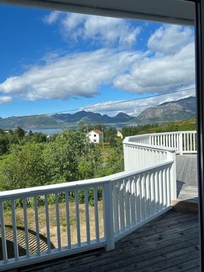 A wooden deck with a white railing overlooking a mountainous landscape and a body of water. - Senja Living (Senja)