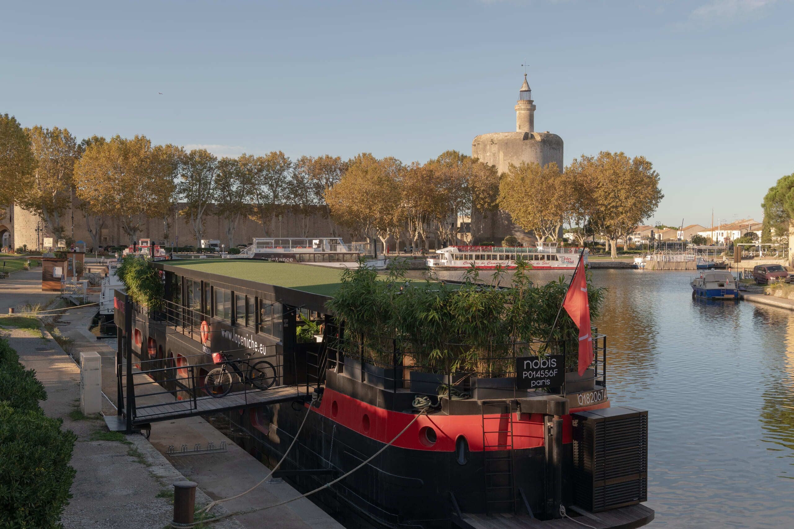 Un restaurant situé au bord de la rivière, avec une terrasse, une vue sur un bâtiment historique et un bateau amarré à proximité.
