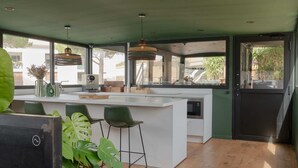 A modern kitchen with a large island, bar stools, pendant lighting, and large windows offering views of the outside.