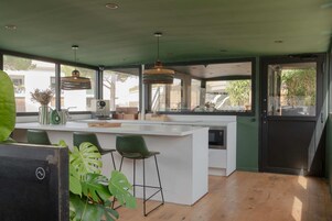 Una cocina moderna con una isla grande, taburetes de bar, iluminación colgante y ventanas amplias que ofrecen vistas al exterior.