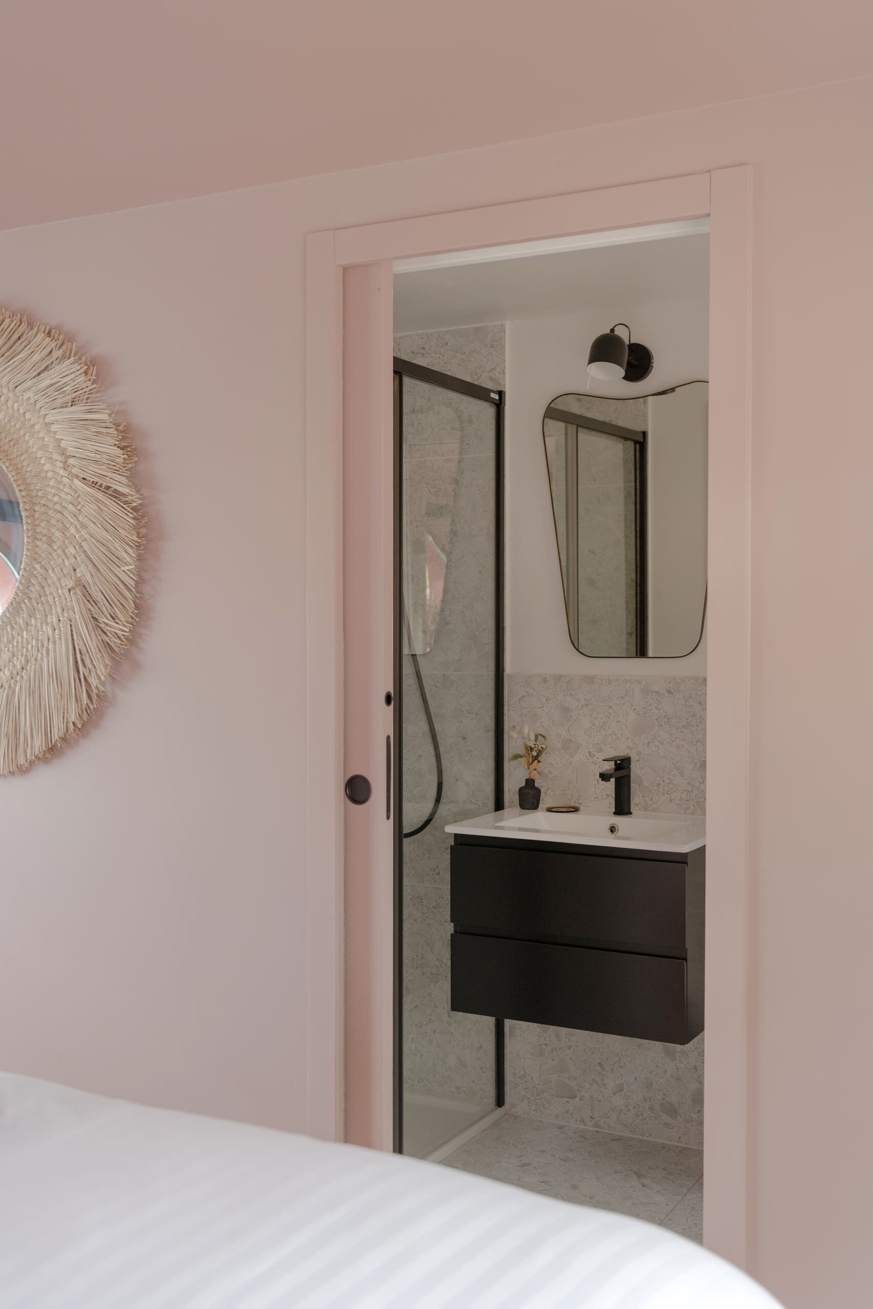 A bedroom with a bed, a door leading to a bathroom with a mirror, a sink, and a towel rack.